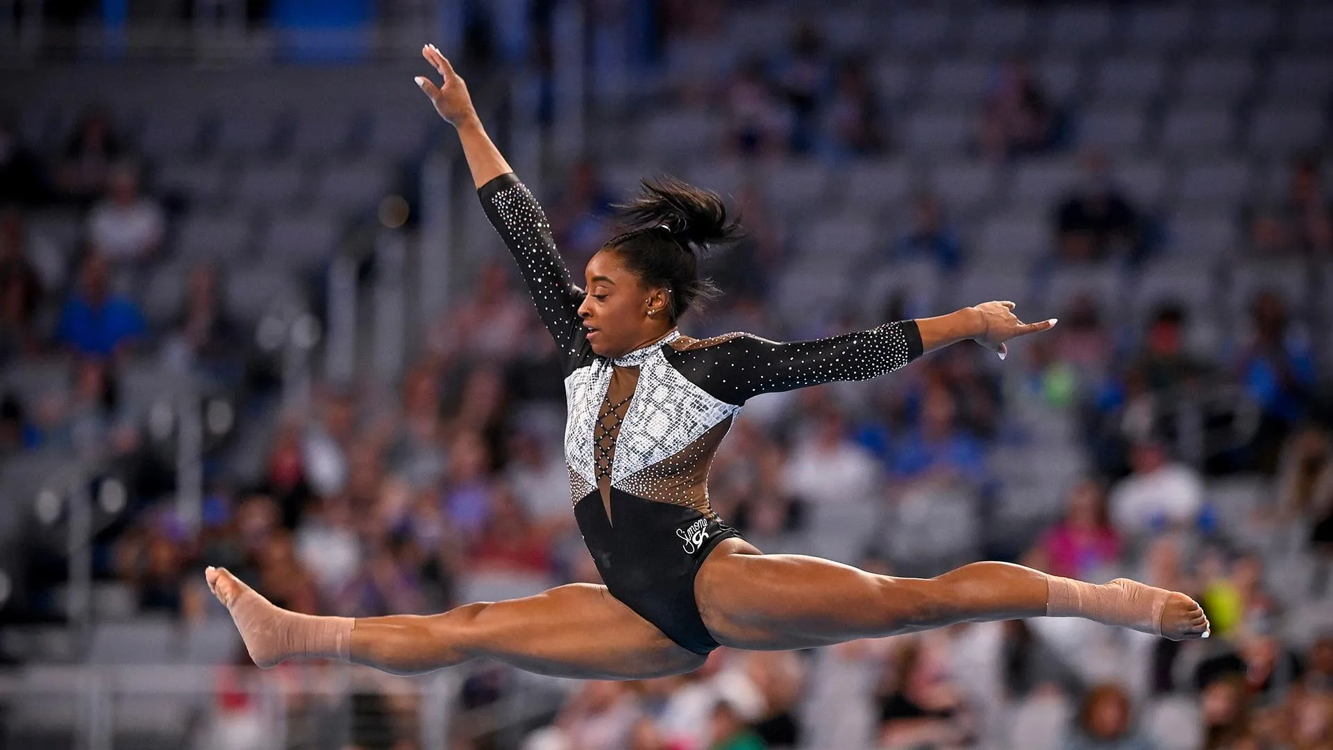 Simone Biles performs a dramatic split leap during a gymnastics competition.